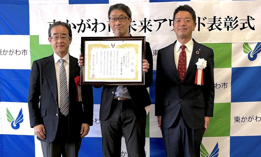 東かがわ市未来アワード表彰式で、賞状を持つ受賞者を中央に、市長と関係者が並んで記念撮影をしている。