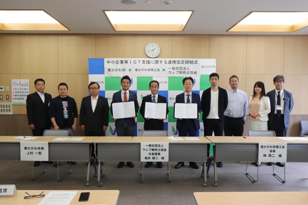 東かがわ市役所で行われた中小企業向けICT支援に関する連携協定締結式。東かがわ市、東かがわ市商工会、一般社団法人ウェブ解析士協会の関係者が横一列に並び、協定書を掲げて記念撮影をしている。